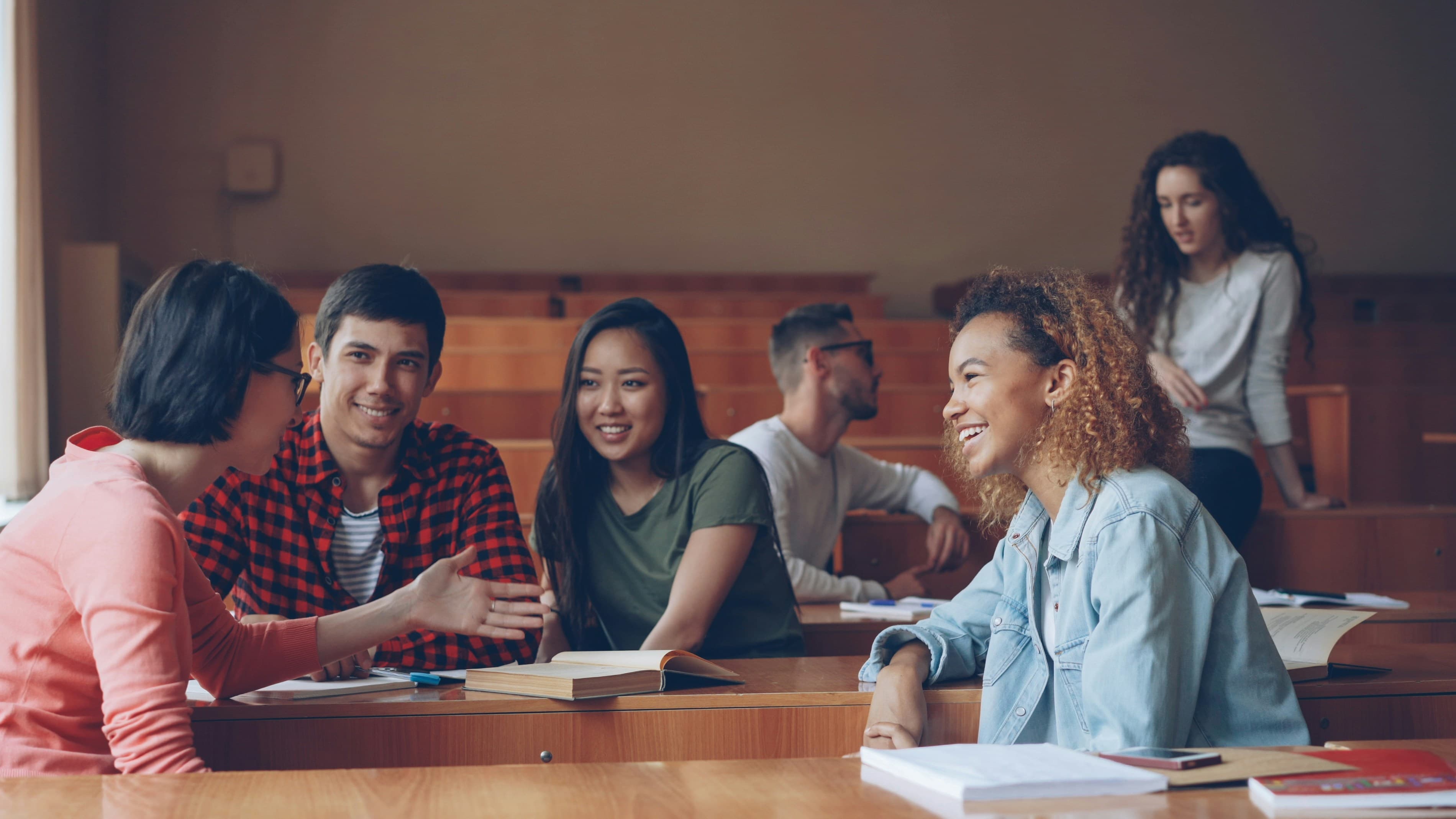 Students talking and laughing across the desks of a lecture hall